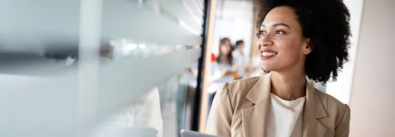 Personne souriante au bureau, tenant un ordinateur portable.