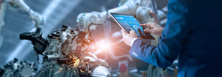 Personne utilisant une tablette pour contrôler un bras robotique en usine.