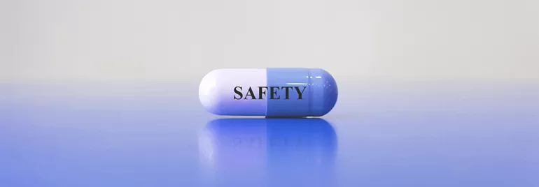 Pilule bicolore avec le mot 'SAFETY' posé sur surface bleue.