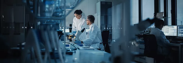Scientifiques en laboratoire examinant un échantillon sous microscope.