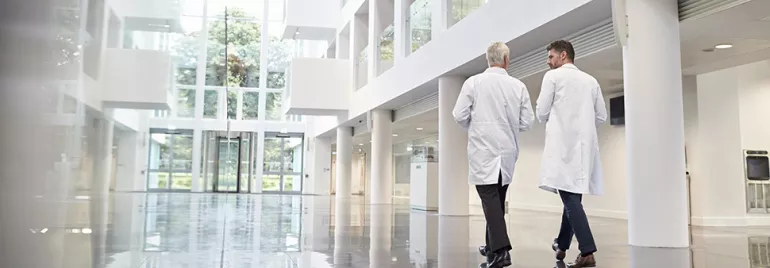 Deux personnes en blouses blanches marchent dans un hall moderne et lumineux.