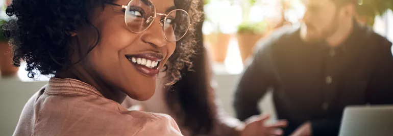 Personne souriante avec des lunettes dans un bureau lumineux.