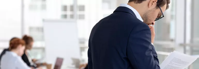 Personne en costume lisant des documents dans un bureau.