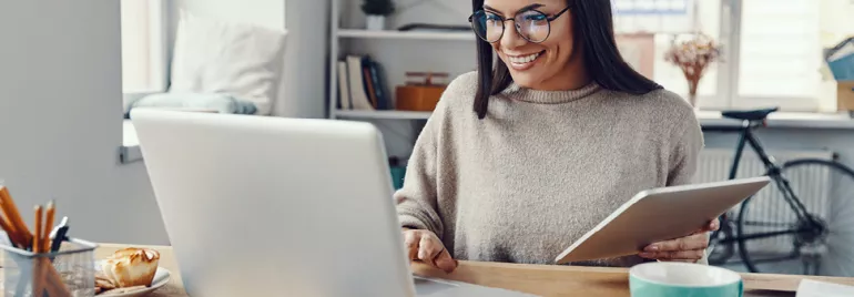 Personne souriante travaillant sur un ordinateur portable avec une tablette.
