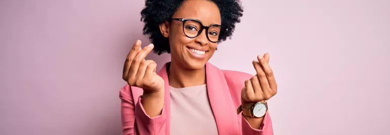 Personne souriante portant des lunettes et un blazer rose, posant devant un arrière-plan rose clair.