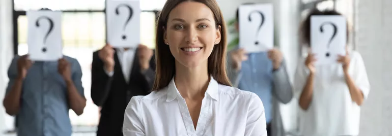Personne souriante au premier plan, autres avec pancartes point d'interrogation en arrière-plan.