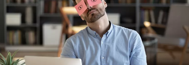 Personne assise à un bureau avec des notes autocollantes sur les yeux.