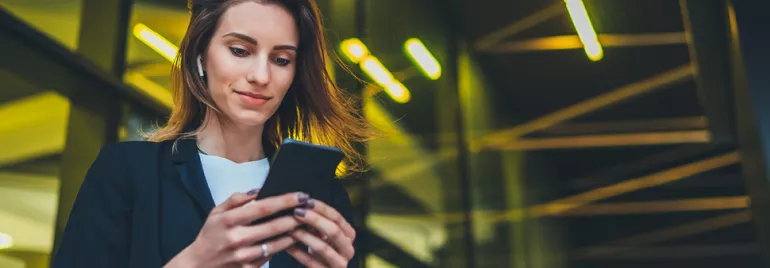 Personne utilisant un smartphone à l'extérieur, écouteurs sans fil.