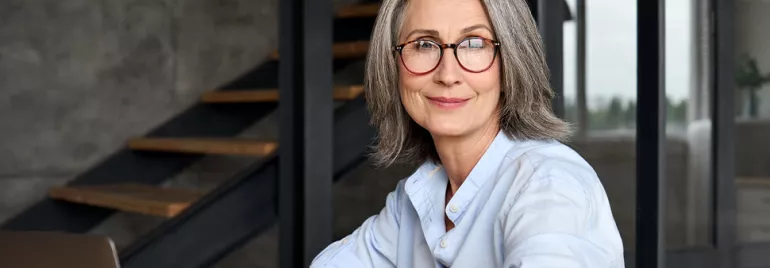 Personne souriante avec des lunettes, assise à une table.