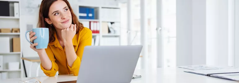 Personne tenant une tasse, rêvant devant un ordinateur portable.