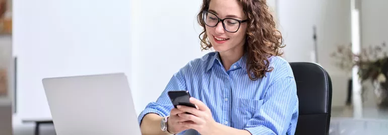 Personne souriante utilisant un smartphone devant un ordinateur portable.