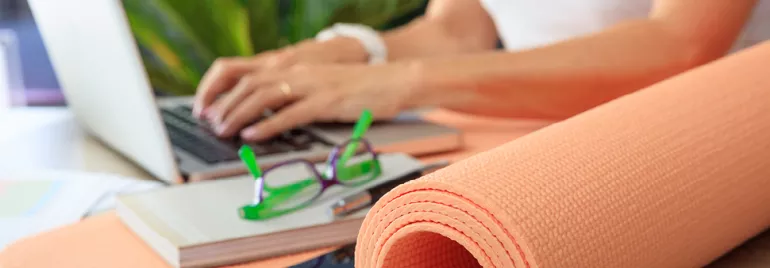 Personne tapant sur un ordinateur portable à côté d'un tapis de yoga et de lunettes.