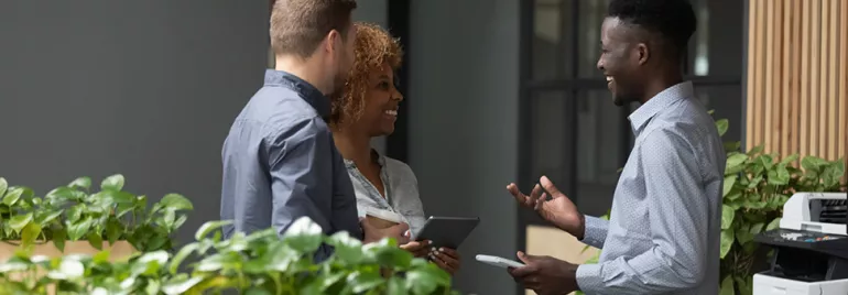 Trois personnes discutent joyeusement près d'une imprimante dans un bureau moderne.