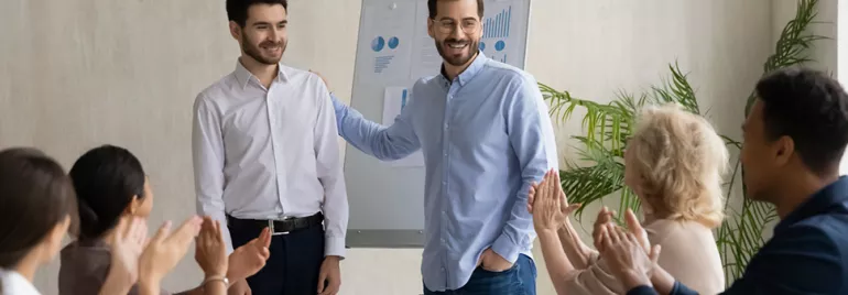 Réunion d'affaires, deux personnes debout souriantes, autres applaudissant.