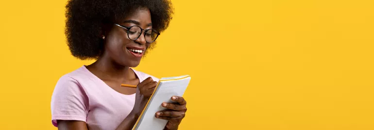 Personne souriante écrivant dans un carnet sur fond jaune.