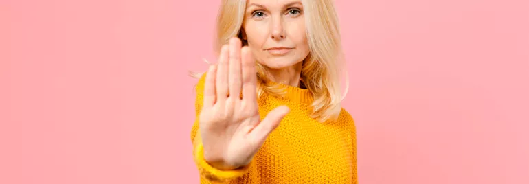 Personne en pull jaune tendant la main sur fond rose.