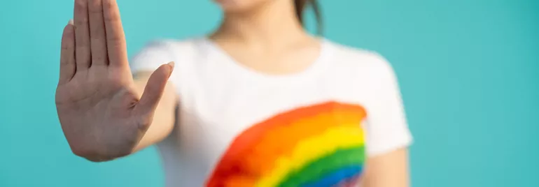 Personne vêtue d'un t-shirt arc-en-ciel levant la main.