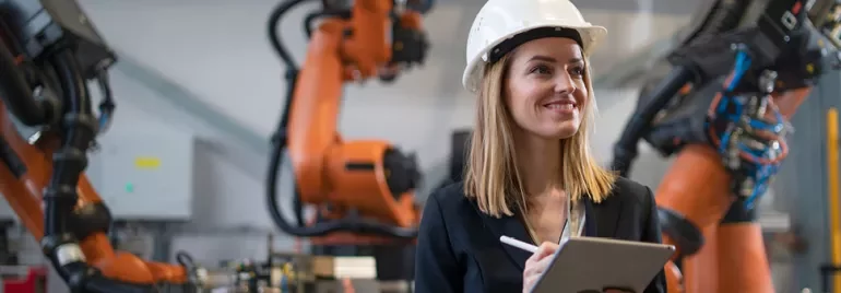 Personne avec un casque tenant une tablette dans une usine avec des robots.