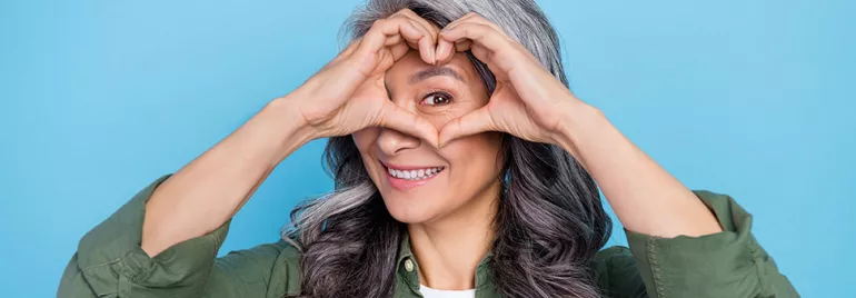 Personne souriante avec les mains formant un cœur devant les yeux.