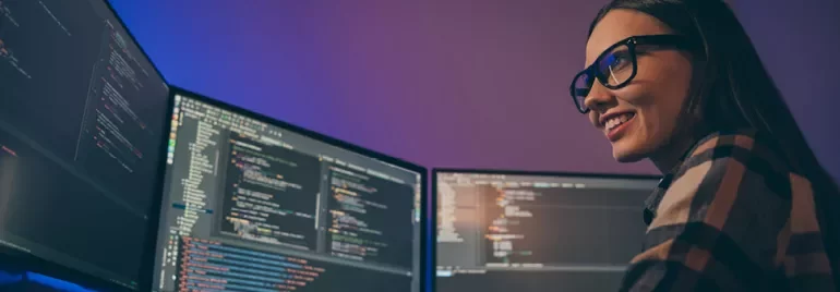 Personne souriante devant plusieurs écrans d'ordinateur avec des lignes de code.