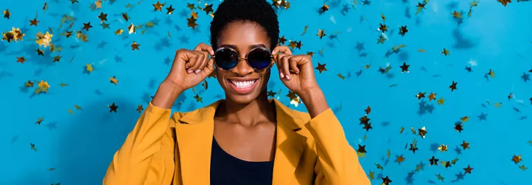 Personne souriante avec des lunettes de soleil devant un fond bleu et des étoiles dorées.