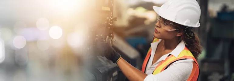 Travailleur en gilet réfléchissant et casque inspectant une machine en usine.