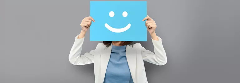 Personne tenant une pancarte avec un visage souriant sur fond gris.
