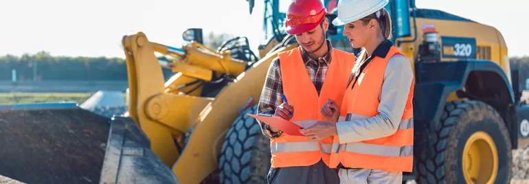 Deux personnes en gilets de sécurité discutant sur un chantier.