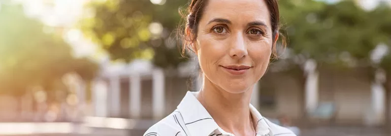 Personne souriante en chemise rayée dans un parc.