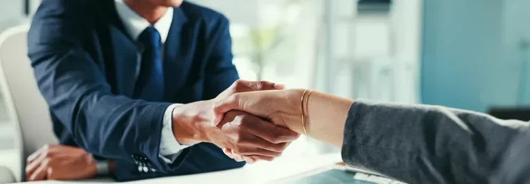 Poignée de mains entre un recruteur et un candidat dans un bureau neutre. Ambiance accord professionnel, tenues business.