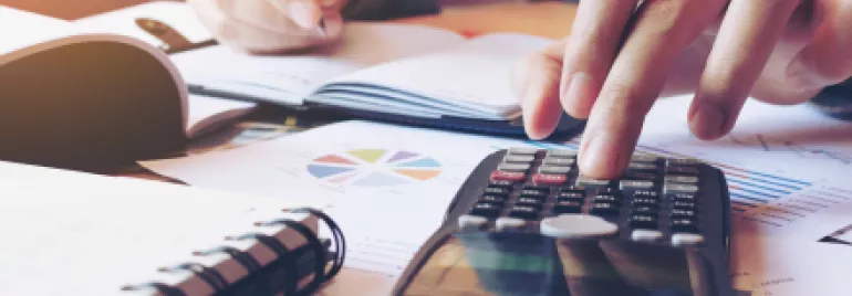 Personne utilisant une calculatrice et écrivant sur des documents.