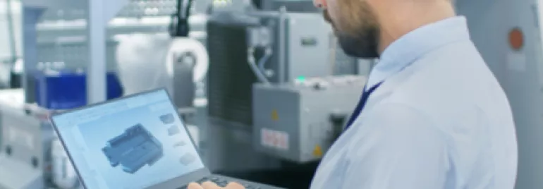 Personne en casque travaillant sur un ordinateur portable dans une usine.