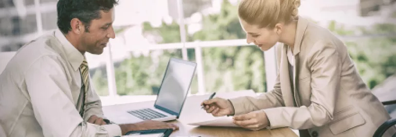 Deux personnes discutent autour d'un bureau avec un ordinateur portable.