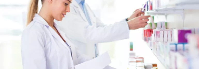 Deux personnes en blouse blanche rangent des médicaments sur des étagères.