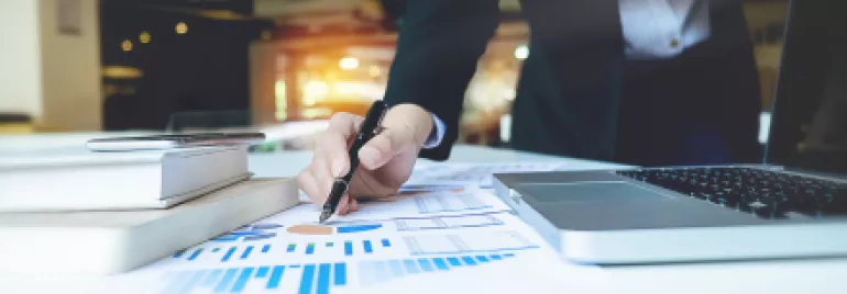 Personne écrivant sur des documents avec un graphique à côté d'un ordinateur portable.