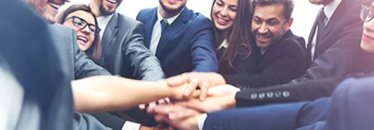 Groupe de collègues souriants se rejoignant les mains.