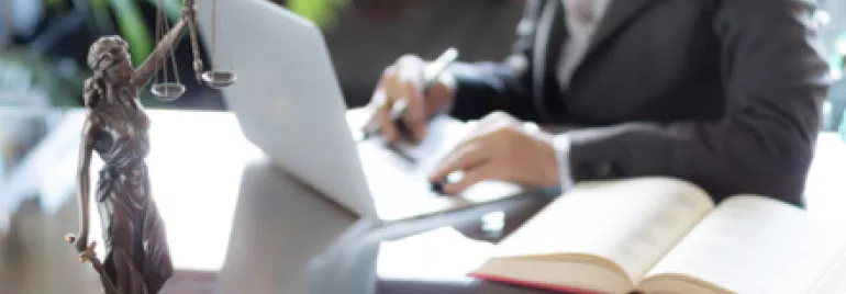 Personne travaillant sur un ordinateur portable avec une statue de justice à l'avant-plan.