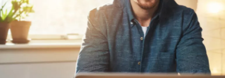 Personne souriante devant un ordinateur portable, lumière naturelle.