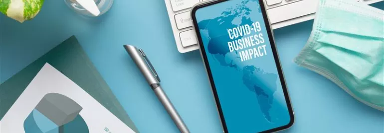Un bureau avec un téléphone affichant 'Impact du COVID-19 sur les affaires'
