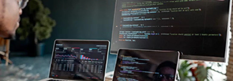 Personne travaillant sur des ordinateurs avec du code affiché sur l'écran.