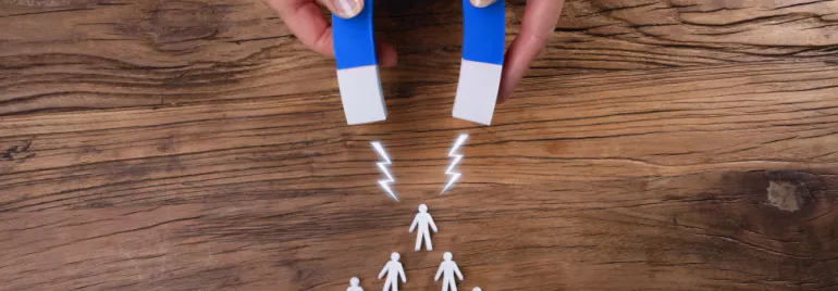 Aimant attirant des silhouettes humaines en plastique sur une table en bois.