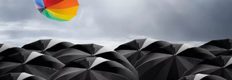 Un parapluie coloré s'envole au-dessus de parapluies noirs.