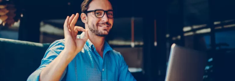 Personne souriant faisant un signe OK devant un ordinateur portable.