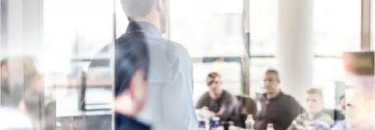Réunion de travail dans une salle vitrée avec plusieurs personnes attentives.