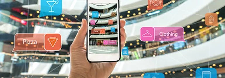 Personne tenant un smartphone dans un centre commercial avec des icônes de restaurants et de magasins en réalité augmentée.