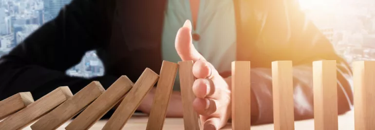 Main arrêtant des dominos en chute sur une table.