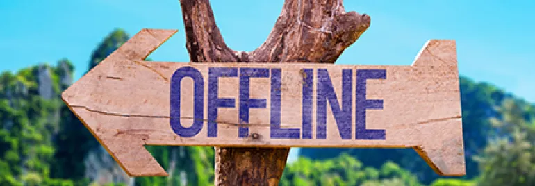 Panneau en bois avec le mot 'OFFLINE', plage et arbres en arrière-plan.