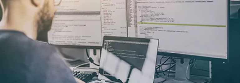 Personne utilisant un ordinateur avec plusieurs écrans affichant du code.