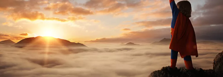 Personne en cape sur une montagne, lever du soleil sur un ciel nuageux.