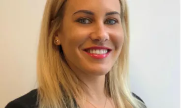Personne souriante portant un blazer noir et un collier doré.